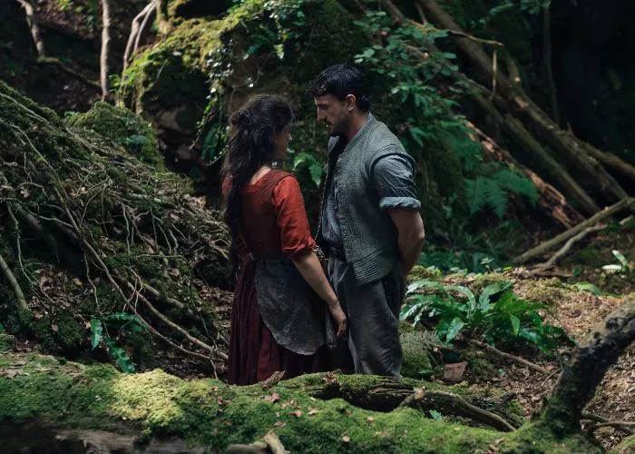 Una scena dal film 'Hamnet' di Chloé Zhao con Jessie Buckley e Paul Mescal in piedi uno di fronte all'altra, in mezzo a una foresta, che si guardano intensamente da molto vicino