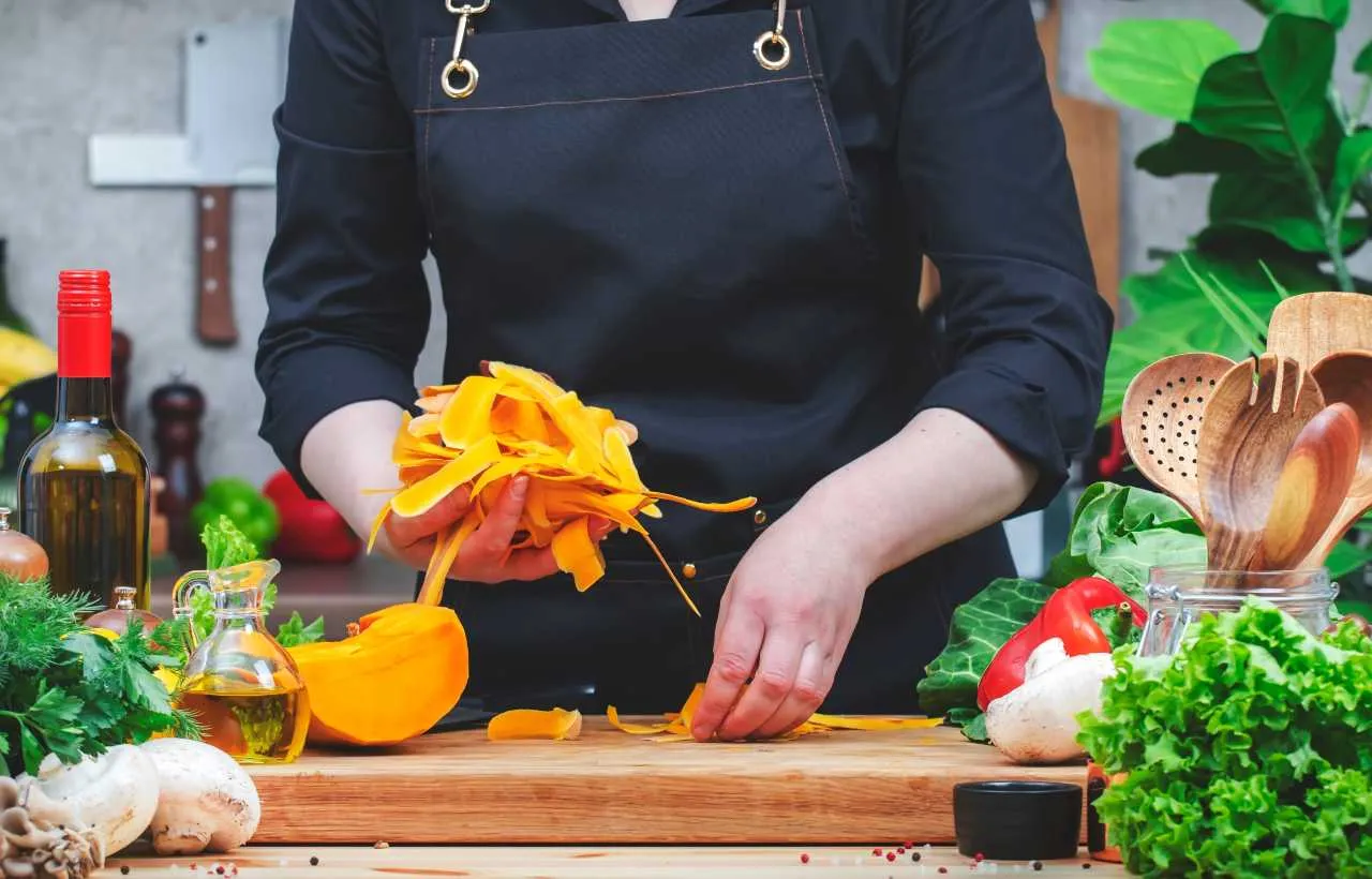 Cuoco in cucina con in mano scarti di zucca per delle ricette zero waste