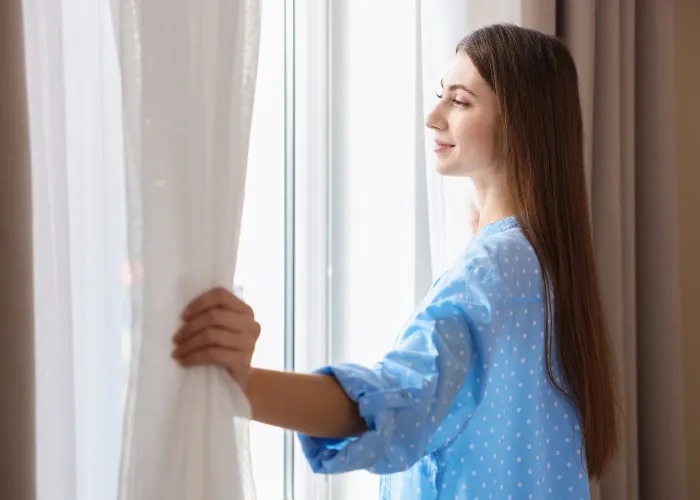 Come eliminare l’umidità in casa - Una ragazza apre tende e finestre a casa