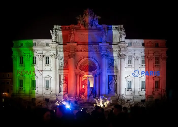 Fontana di Trevi illuminata di notte con bandiere di Italia e Francia per il 70° anniversario del gemellaggio tra Parigi e Roma
