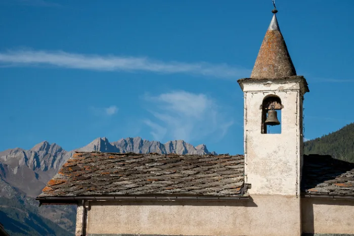 Chiesa con campanile e tetto in pietra a Étroubles, con le cime della Valle d'Aosta sullo sfondo