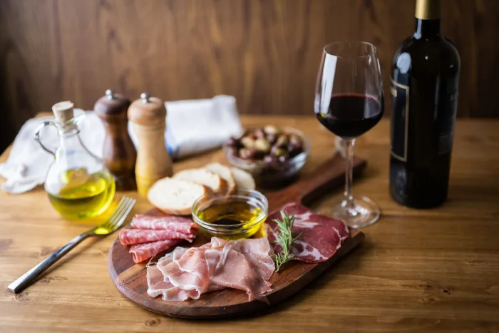 Tagliere di salumi con olio e un bicchiere di vino rosso, tipico di un'osteria italiana