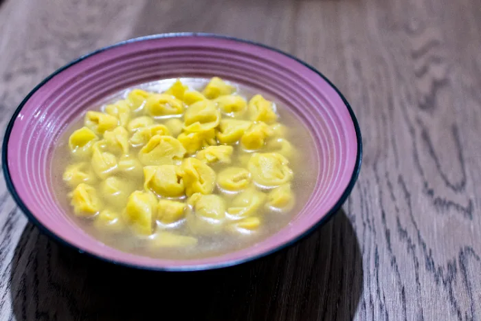Una ciotola di tortellini nel brodo di pollo fumante, sul tavolo di legno