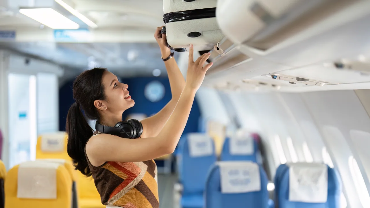 Viaggiatrice sorridente che sistema il bagaglio a mano sulla cappelliera dell'aereo