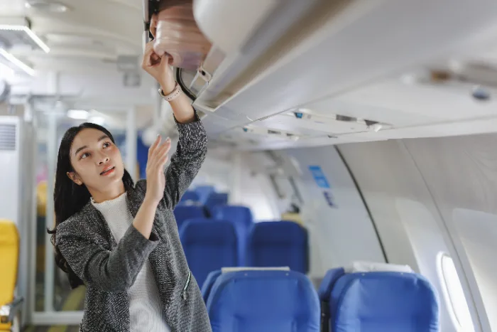 Donna che sistema il bagaglio nella cappelliera dell'aereo. Bagagli a mano gratis su easyJet, Ryanair e Wizz Air.